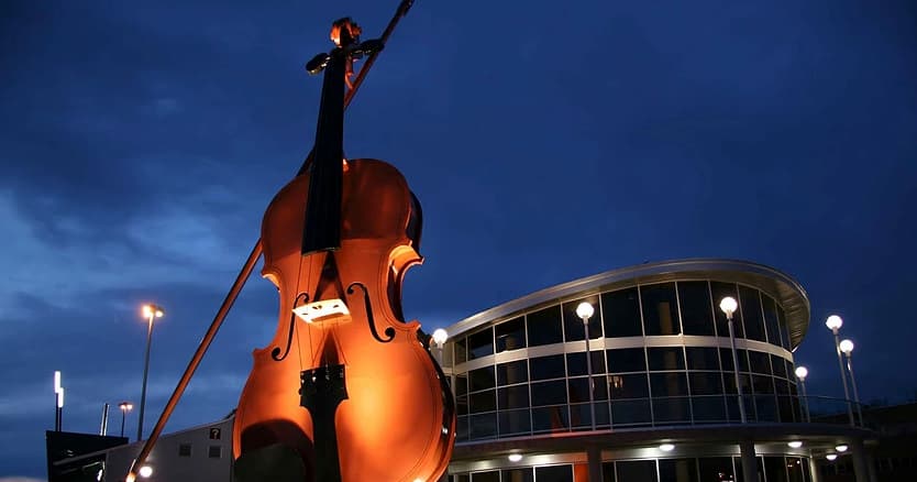 Giant upright bass sculpture lit at night outside concert hall