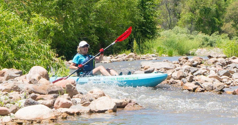 Kayaker navigating rocky river shallow rapids near green trees