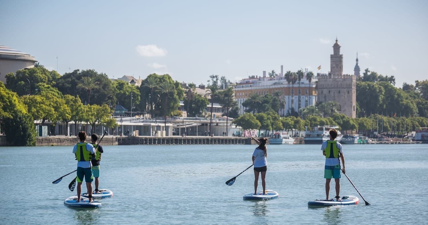 Three paddleboarders crossing Guadalquivir River skyline
