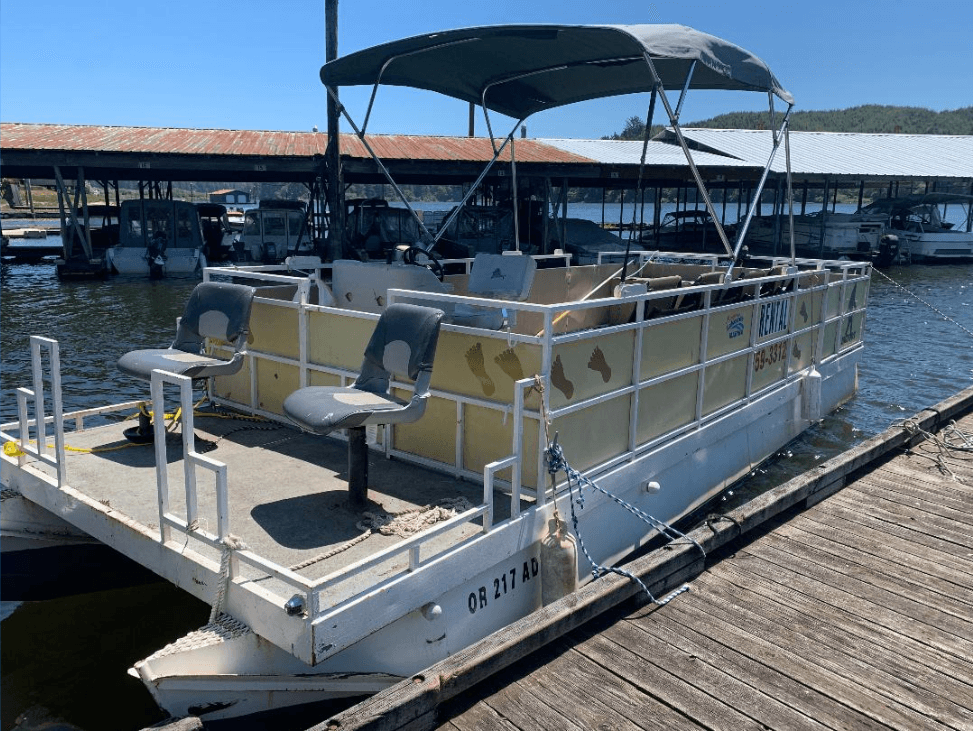 Covered yellow pontoon boat moored at lakeside rental dock