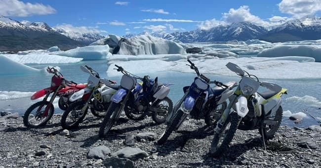 Dirt bikes parked by glacial lagoon with mountains in Alaska