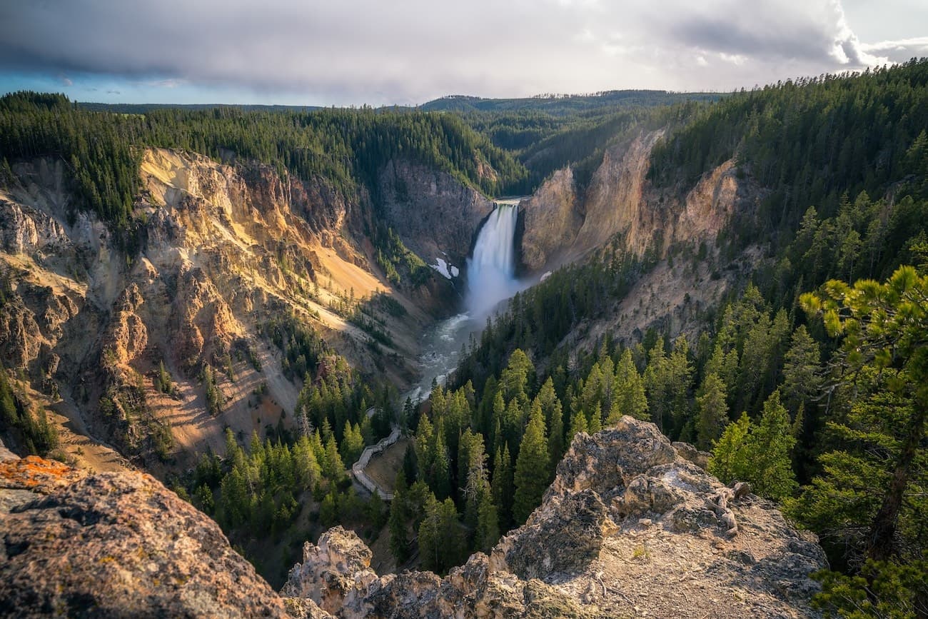Waterfall plunging into a forested valley in dramatic light