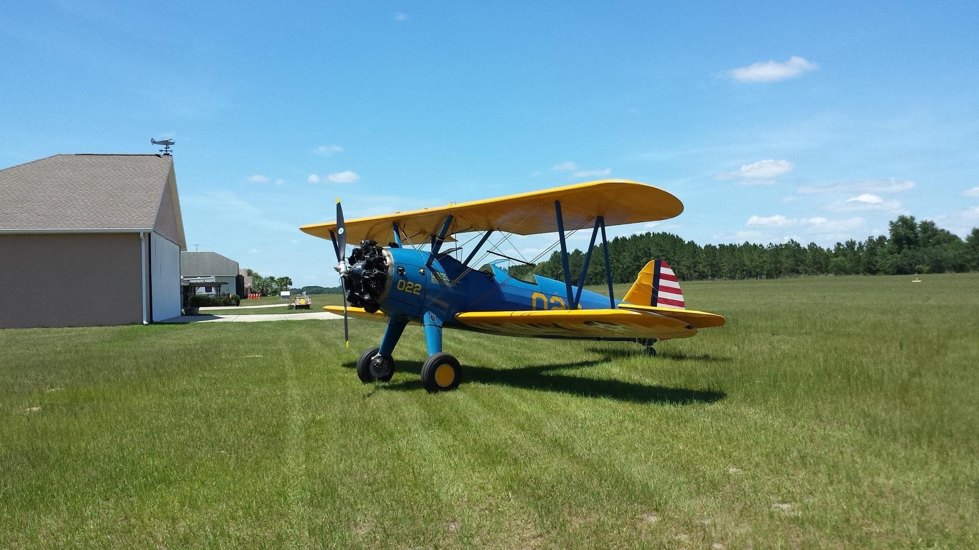 Parked yellow-blue biplane on grass airfield near hangar under sky