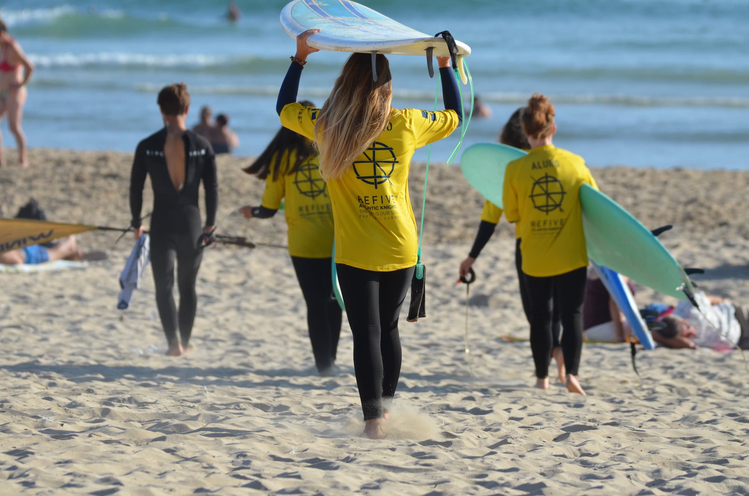 Surfers carrying boards across sandy beach toward ocean lineup