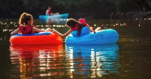Two people tubing together on calm river summer float trip