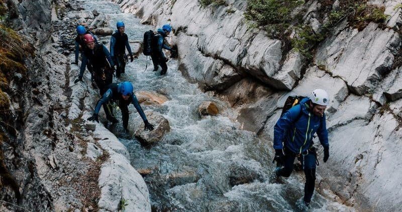 Group canyoning through rocky mountain stream, narrow canyon