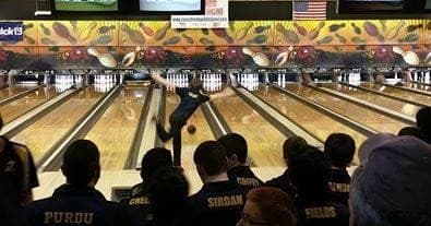 Competitive bowler releasing strike shot at indoor bowling alley lane