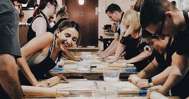 Group cooking class rolling dough in indoor culinary workshop