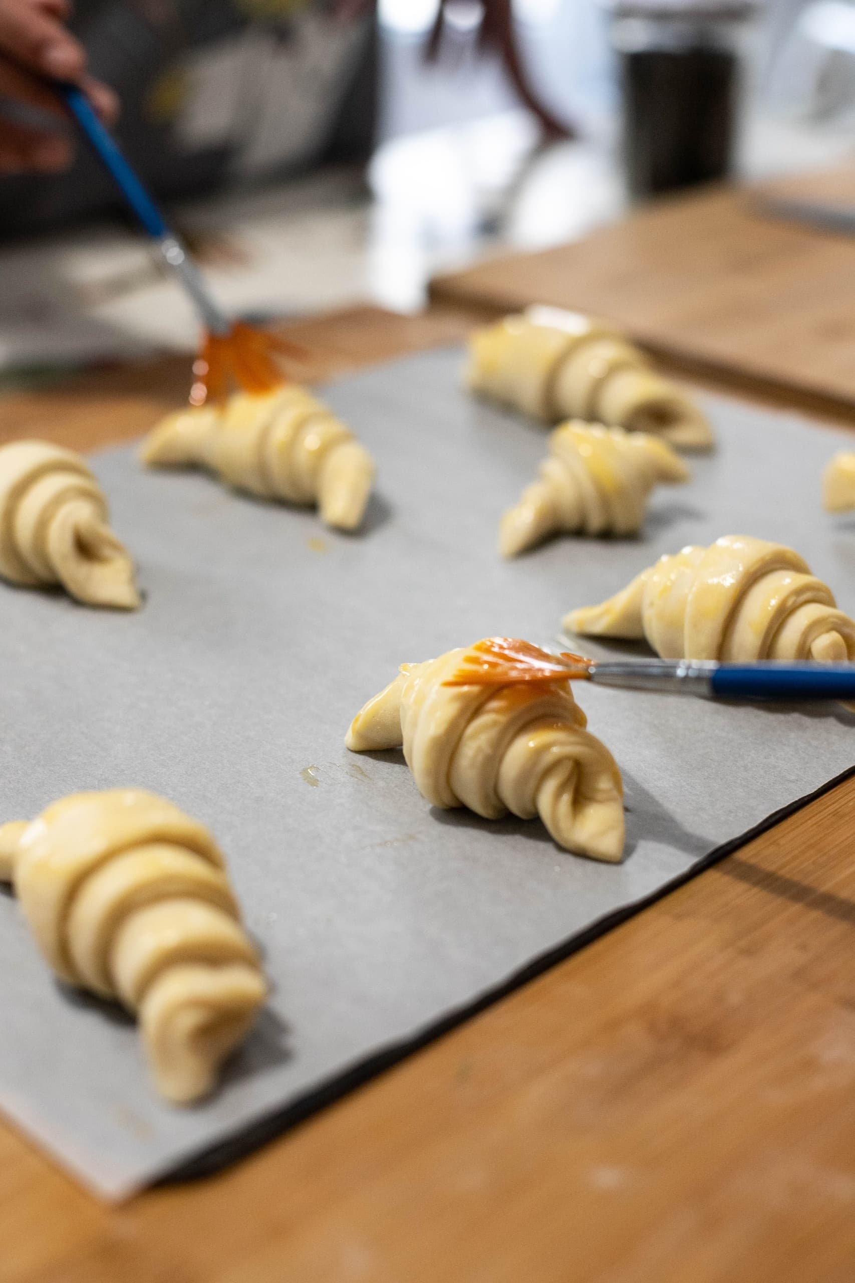 Croissants lined on parchment being brushed before baking in bakery