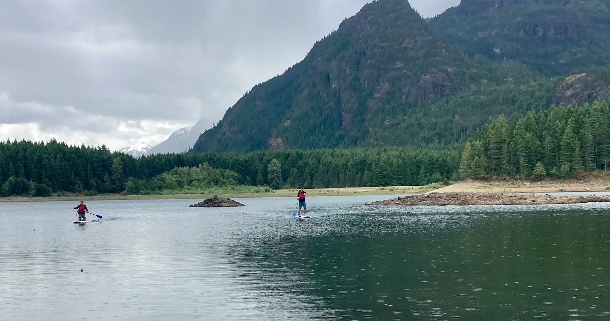 Paddleboarders on calm mountain lake with forested shoreline