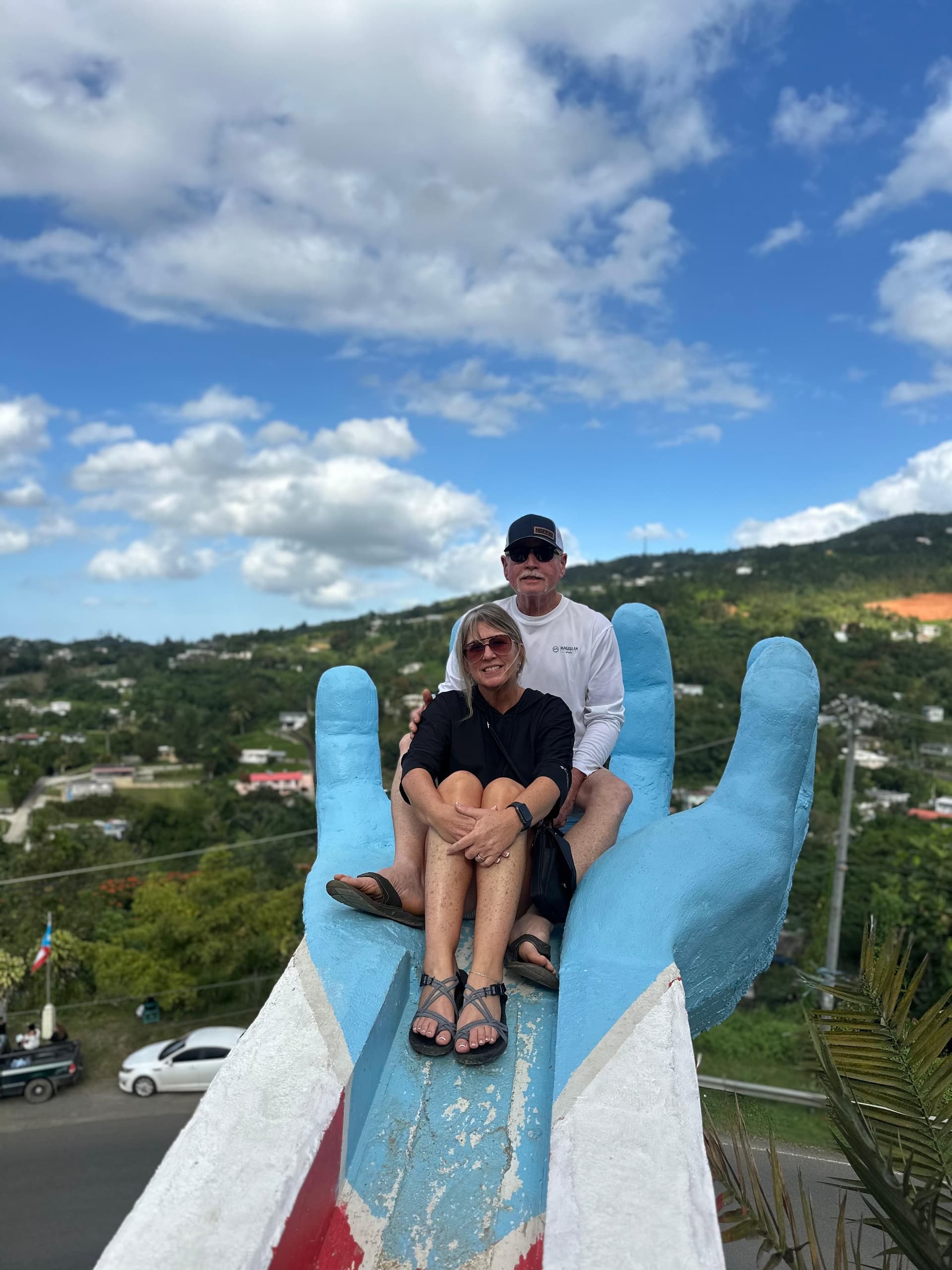 Couple on giant hand overlook with island vista and sky