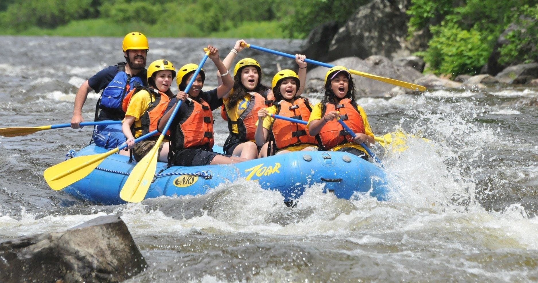 Guided whitewater rafting group charging down rocky river rapids