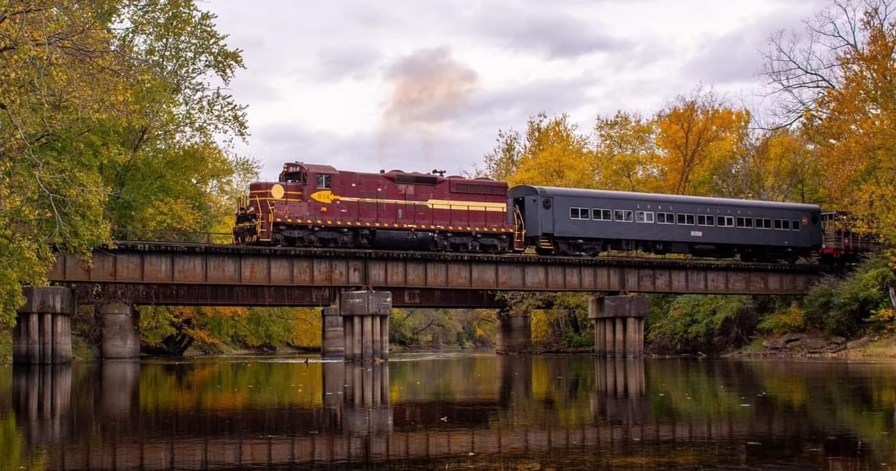 Vintage train crossing river bridge amid fall foliage with reflections