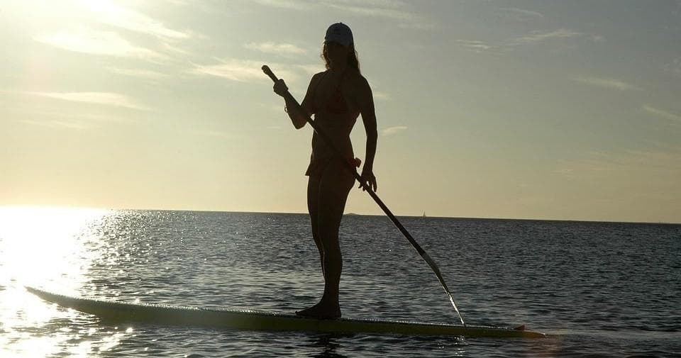 Stand-up paddleboarder silhouetted at sunset on open water