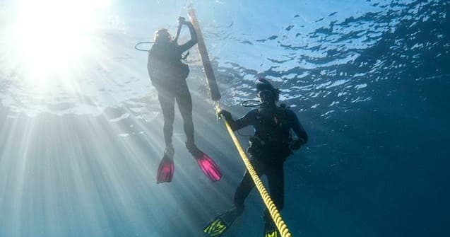 Scuba divers ascending near rope with sun rays, Menorca