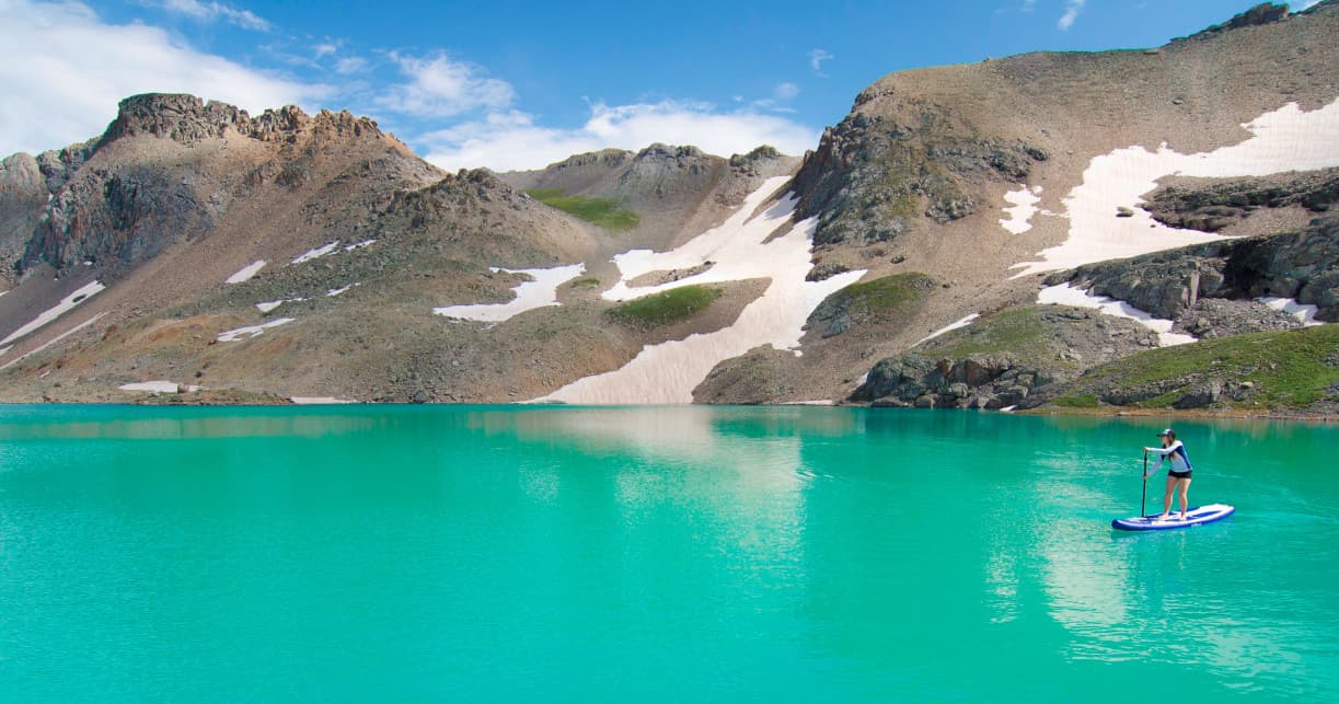 Standup paddleboarder on turquoise alpine lake beneath peaks