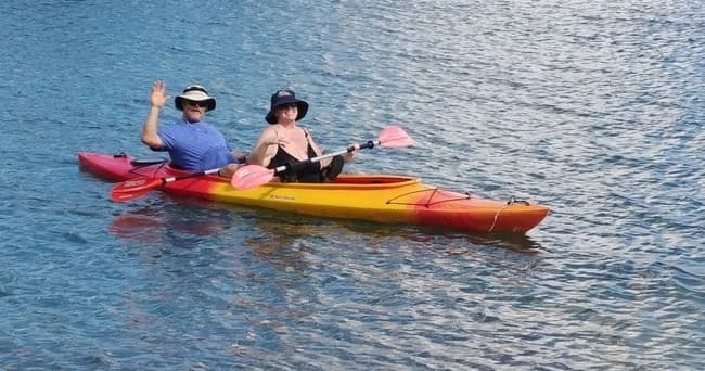 Two-person tandem kayak paddling on calm blue bay near shore