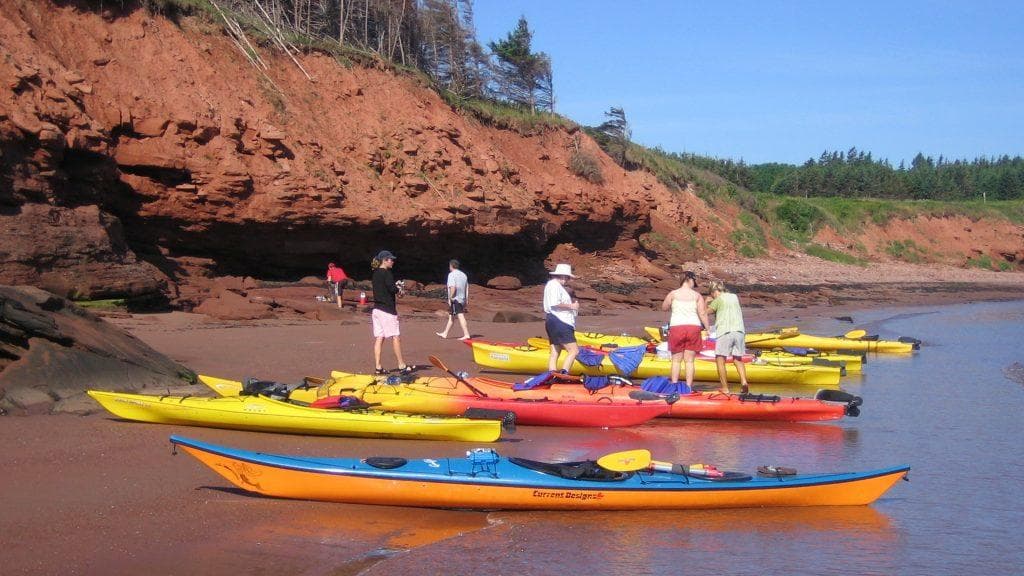 Colorful sea kayaks beached on red sand with rocky cliffs