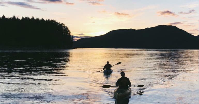 Kayakers paddling at sunset in Alaskan coastal inlet