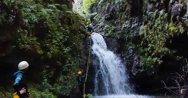 Canyoneers rappelling beside a waterfall in Madeira canyon