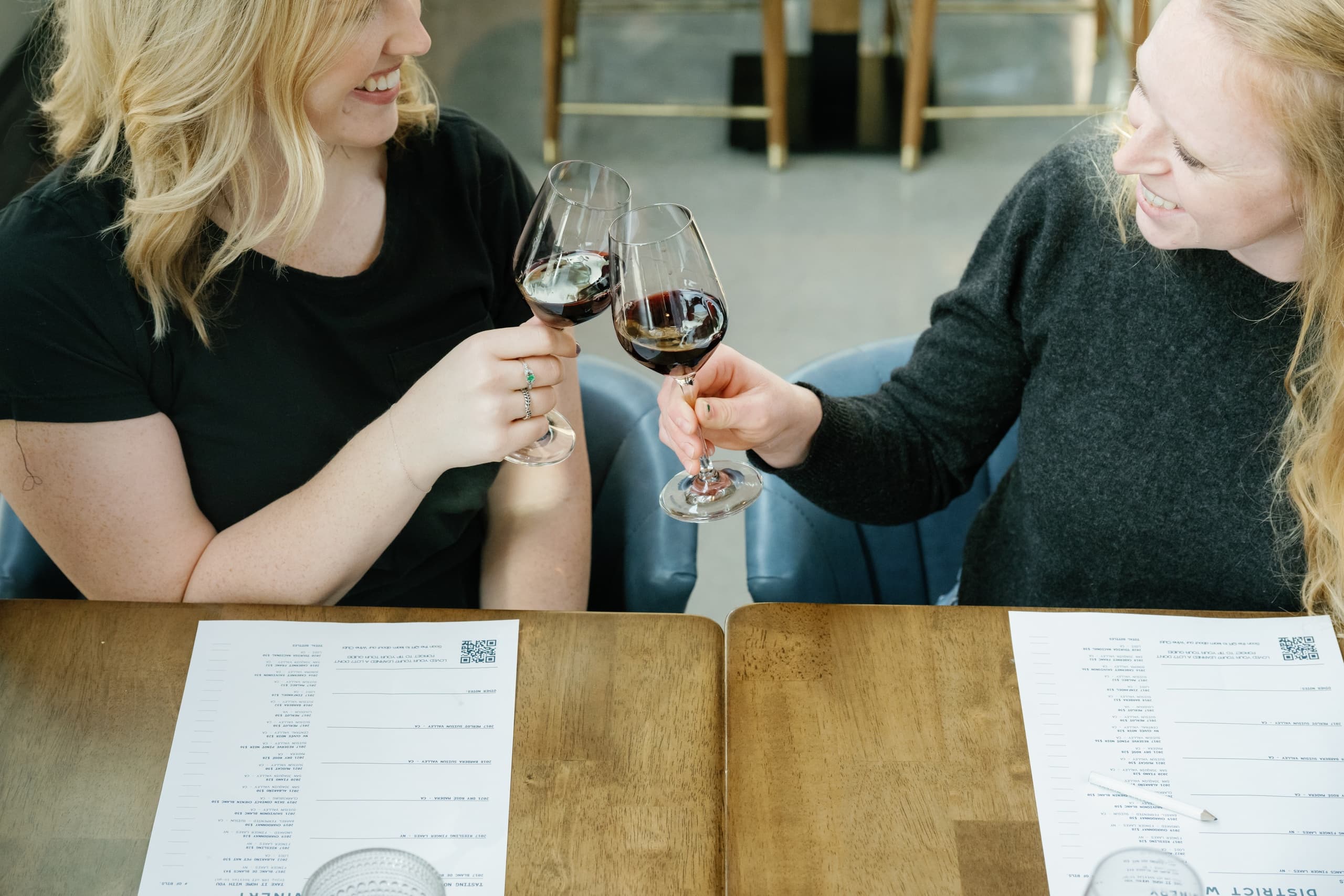 Friends clinking red wine glasses at tasting table indoors