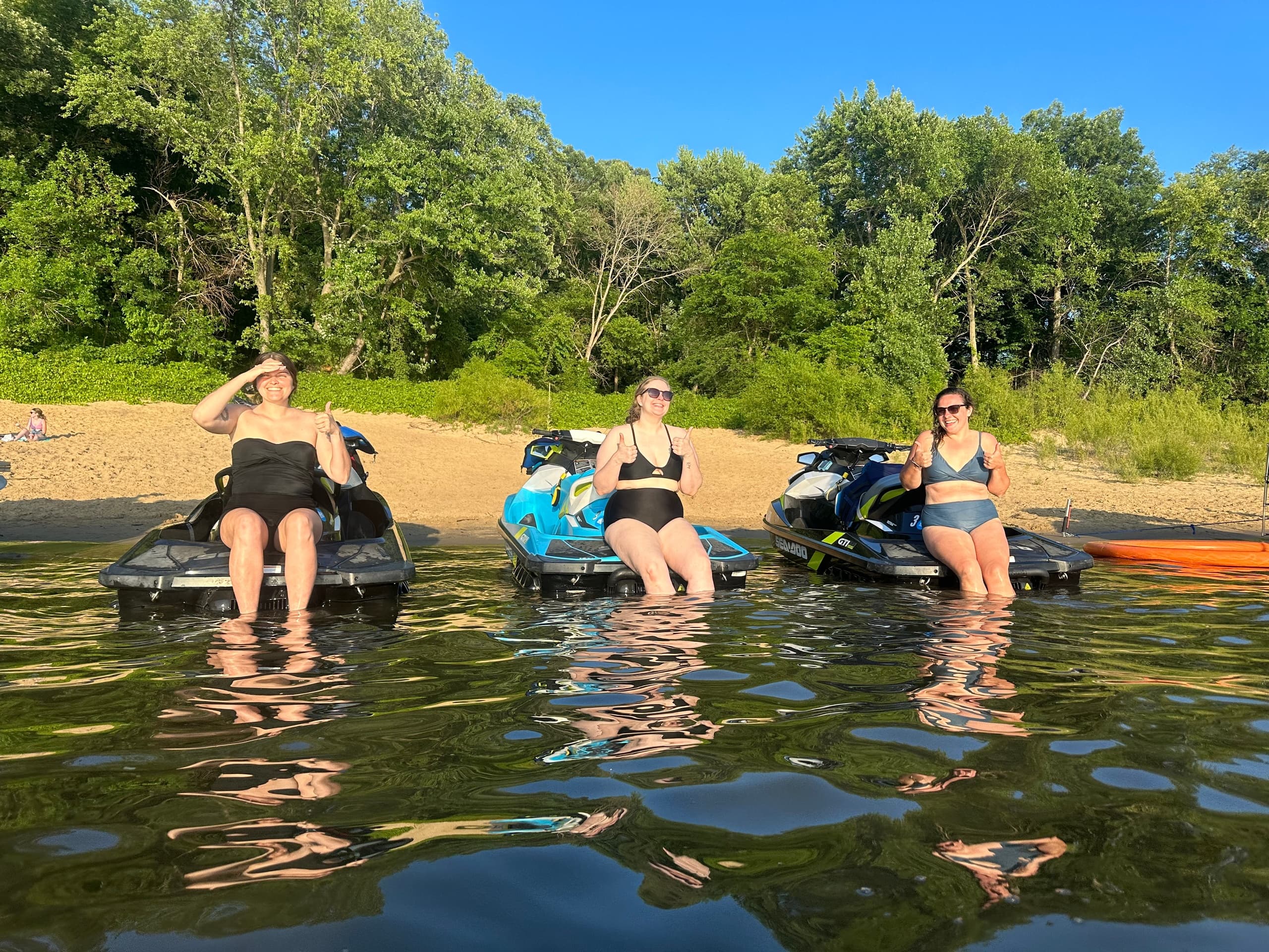 Three riders on jet skis at a forested lakeshore enjoying summer
