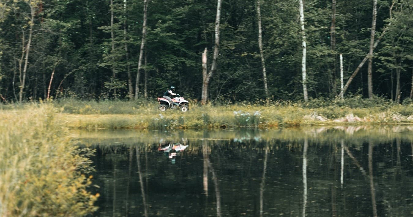 ATV parked by reflective pond in mixed forest clearing