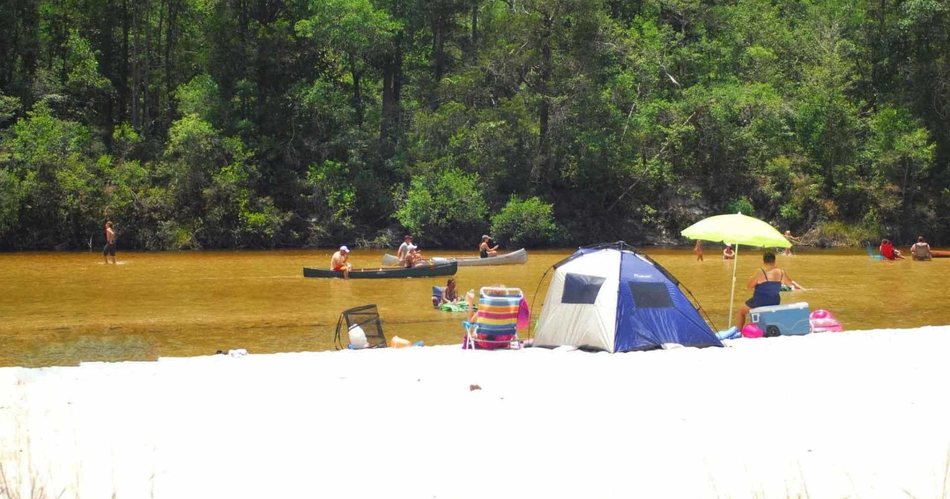 Riverside camping with tent and umbrella on sandy bank