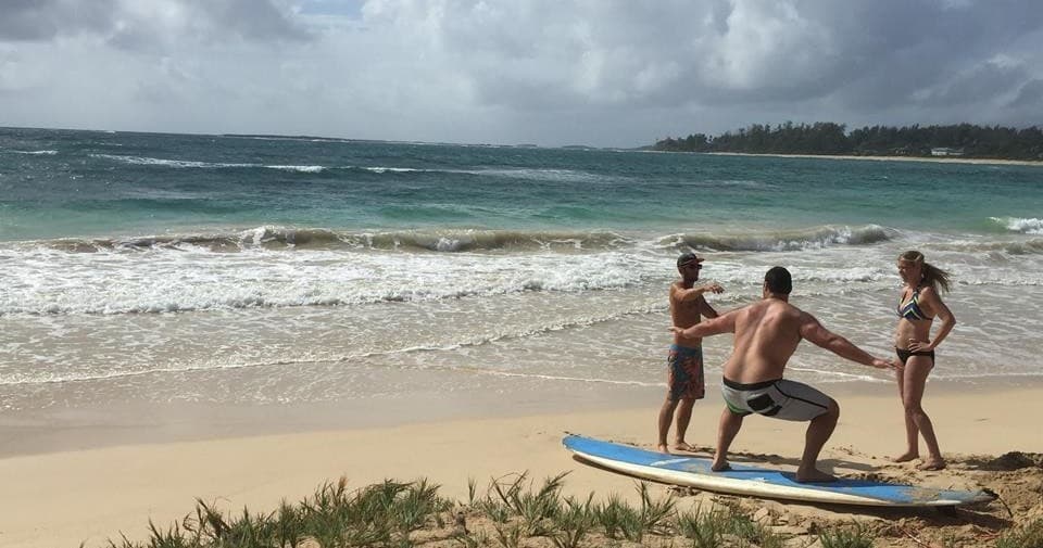 Surf lesson group practicing standing drills on sandy beach with waves
