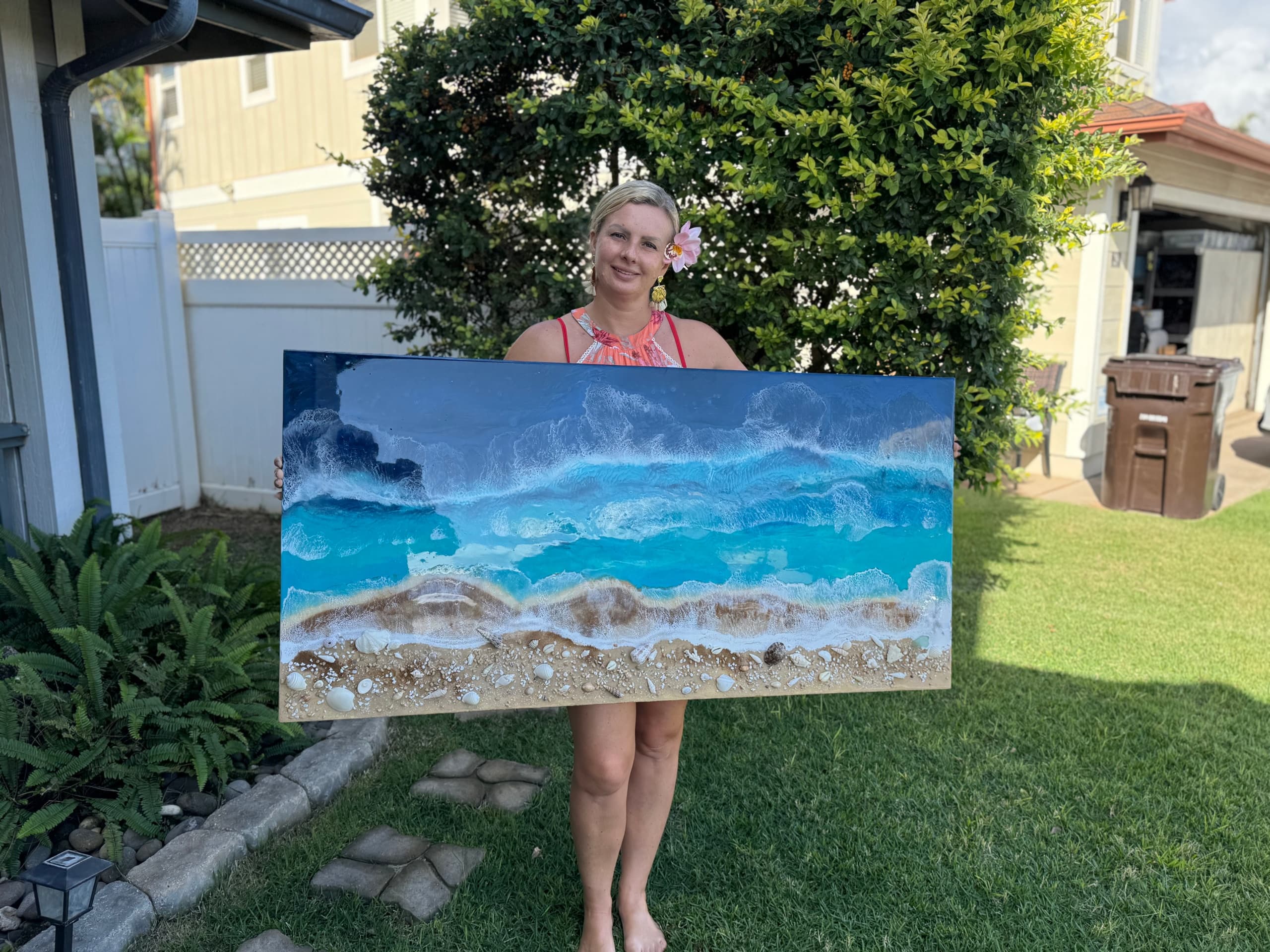 Artist holding large ocean painting outdoors in backyard