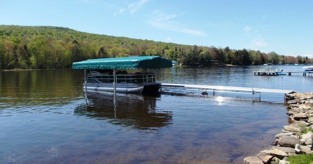 Covered pontoon docked on scenic forested lake shoreline