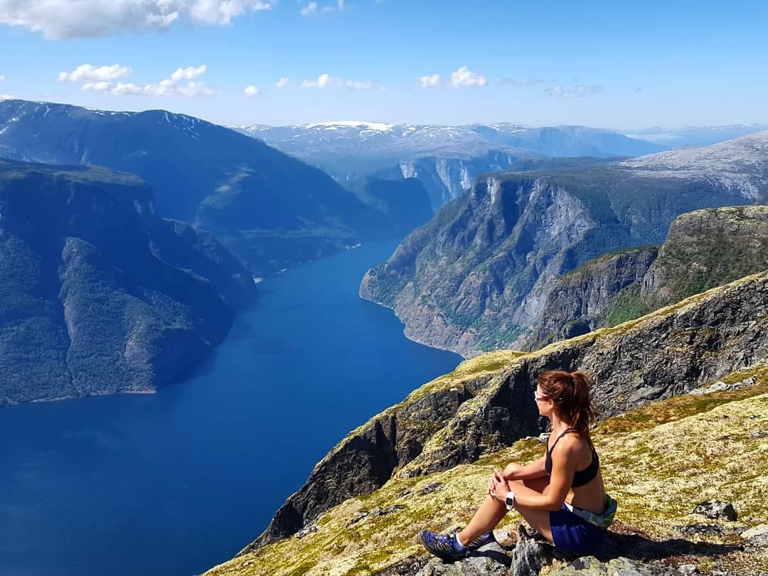 Solo hiker sitting on fjord cliff overlooking deep blue water