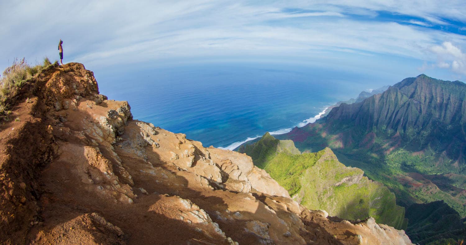 Hiker on cliff overlooking lush Kauai coastline and ocean