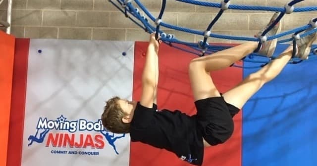 Child climbing indoor cargo net at ninja gym training