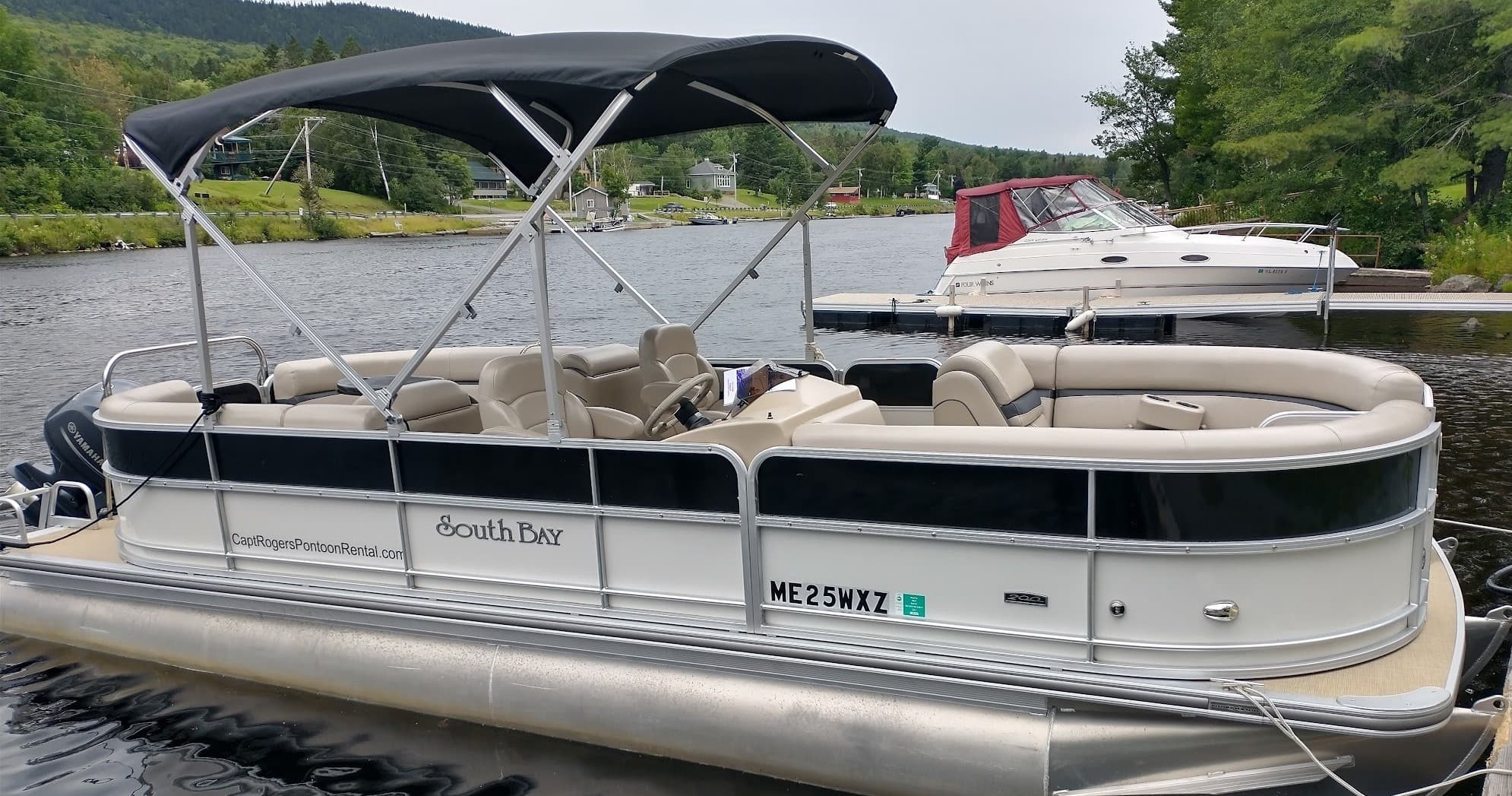 Beige pontoon boat with canopy on lake near forested shore