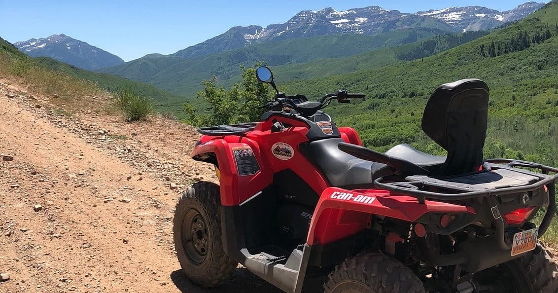 Red ATV parked on mountain dirt trail with green valley