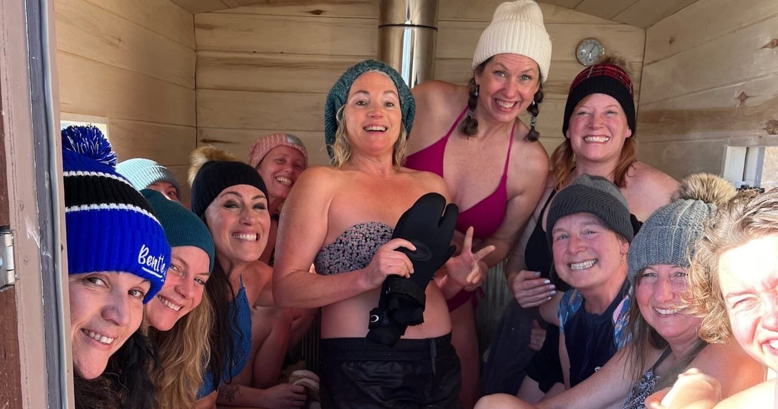 Group in portable sauna cabin doorway smiling after outdoor winter swim