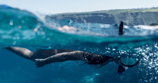 Snorkeler swimming beneath turquoise Hawaiian coastal waters