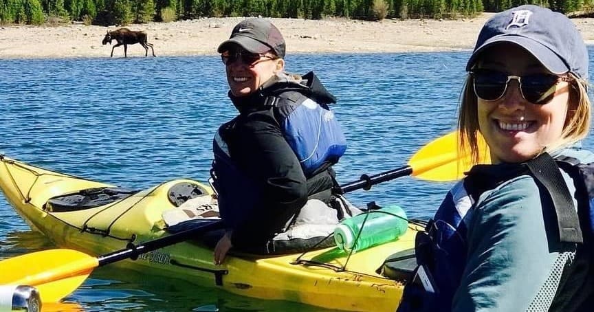 Two smiling kayakers on clear coastal water wearing life vests