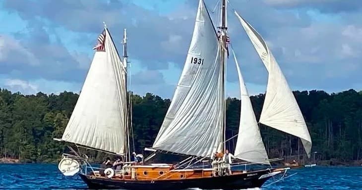 Classic sailboat with full sails cruising on blue lake