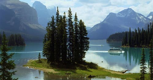 Emerald lake with tree-covered island and mountain vistas at dusk