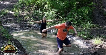 Participants wading through muddy forest trail during an adventure run