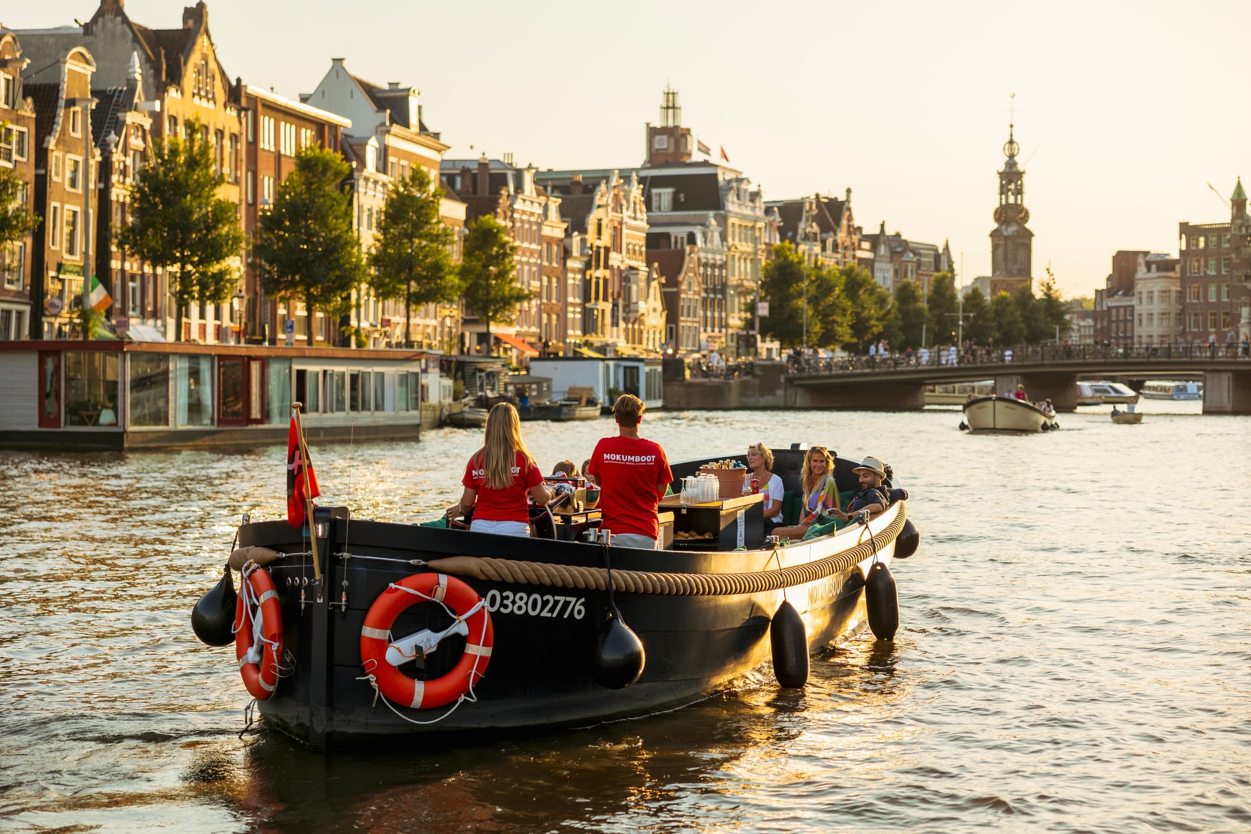 Small boat cruising Amsterdam canal past historic canal houses