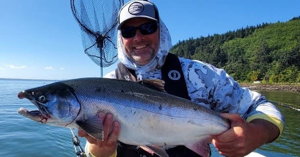 Angler holding large salmon on coastal boat near forested shore