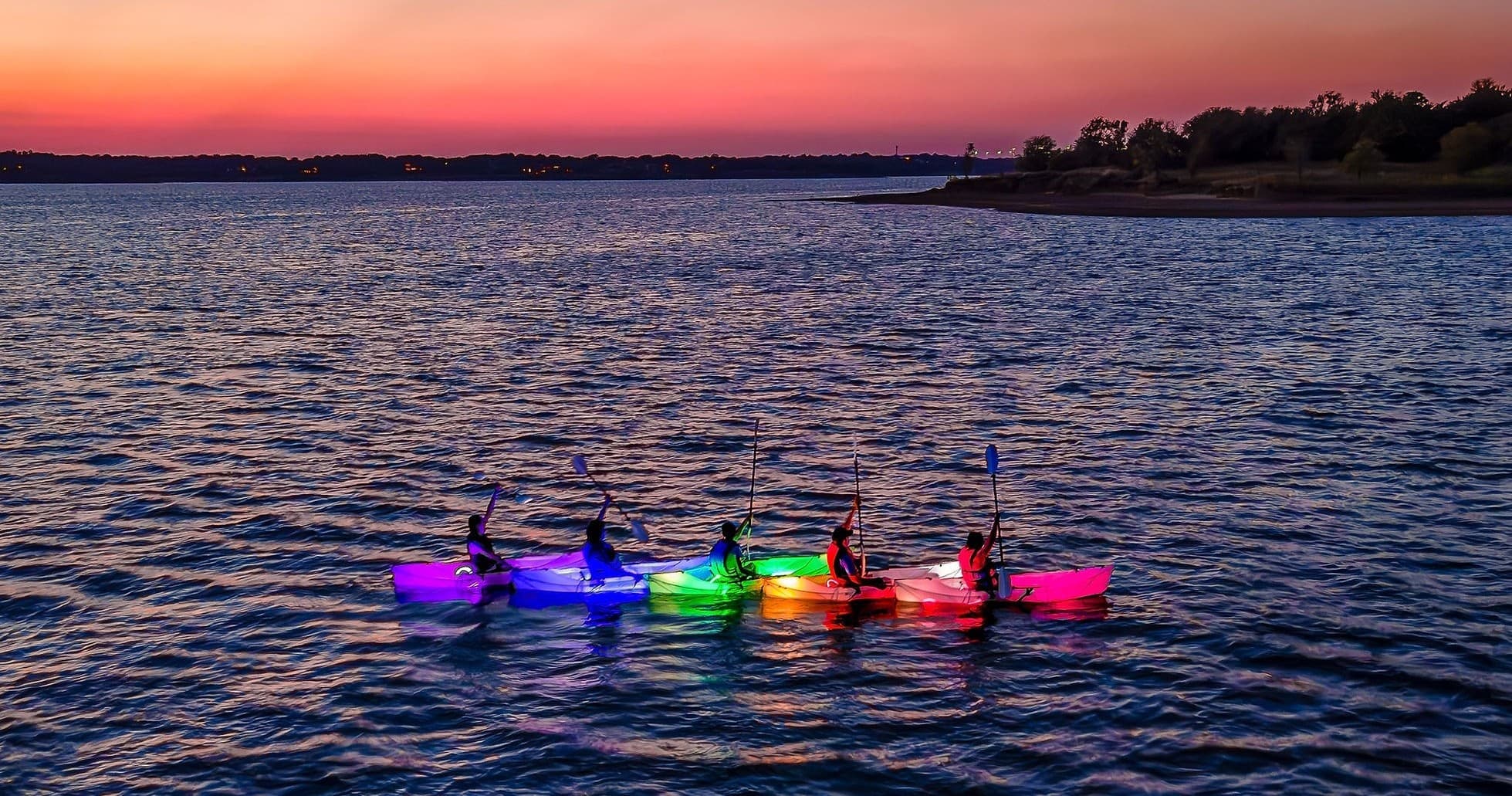 Glow kayak tour: paddlers in illuminated kayaks at lake sunset
