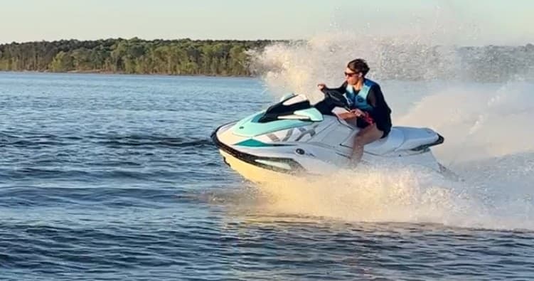 Jet ski rider racing across open lake water with spray and wake