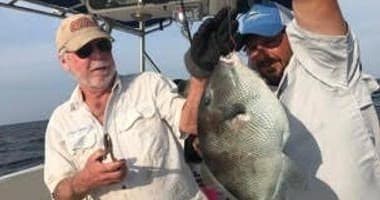Two anglers proudly holding large caught fish aboard charter boat