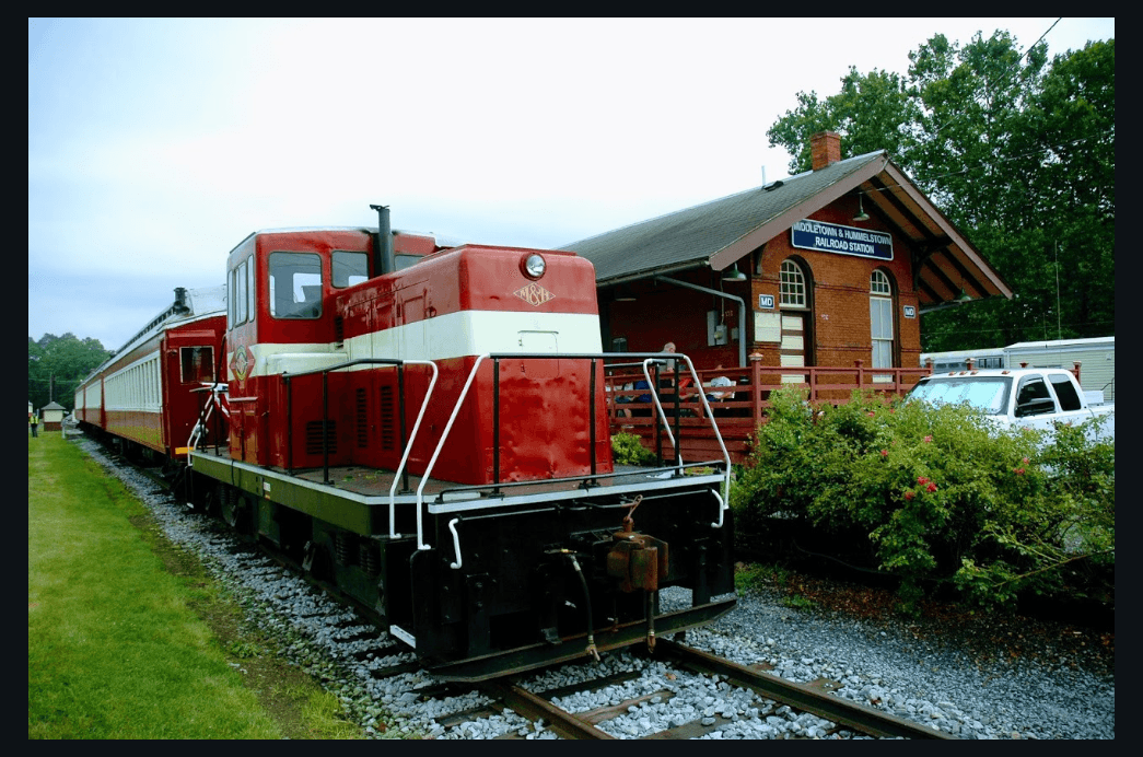 Red locomotive parked beside historic wooden rail depot