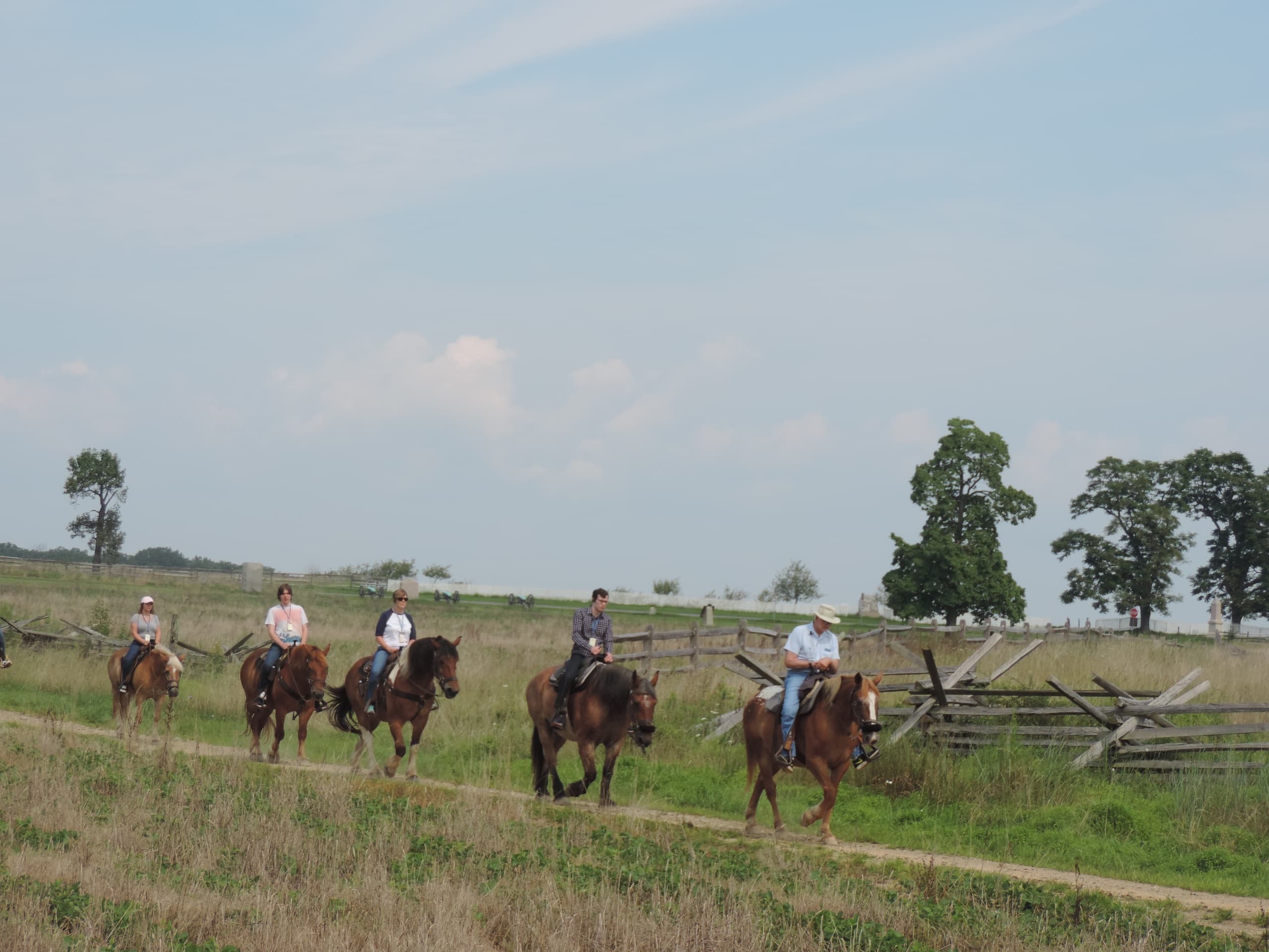 Group horseback riders on grassy trail across open farmland
