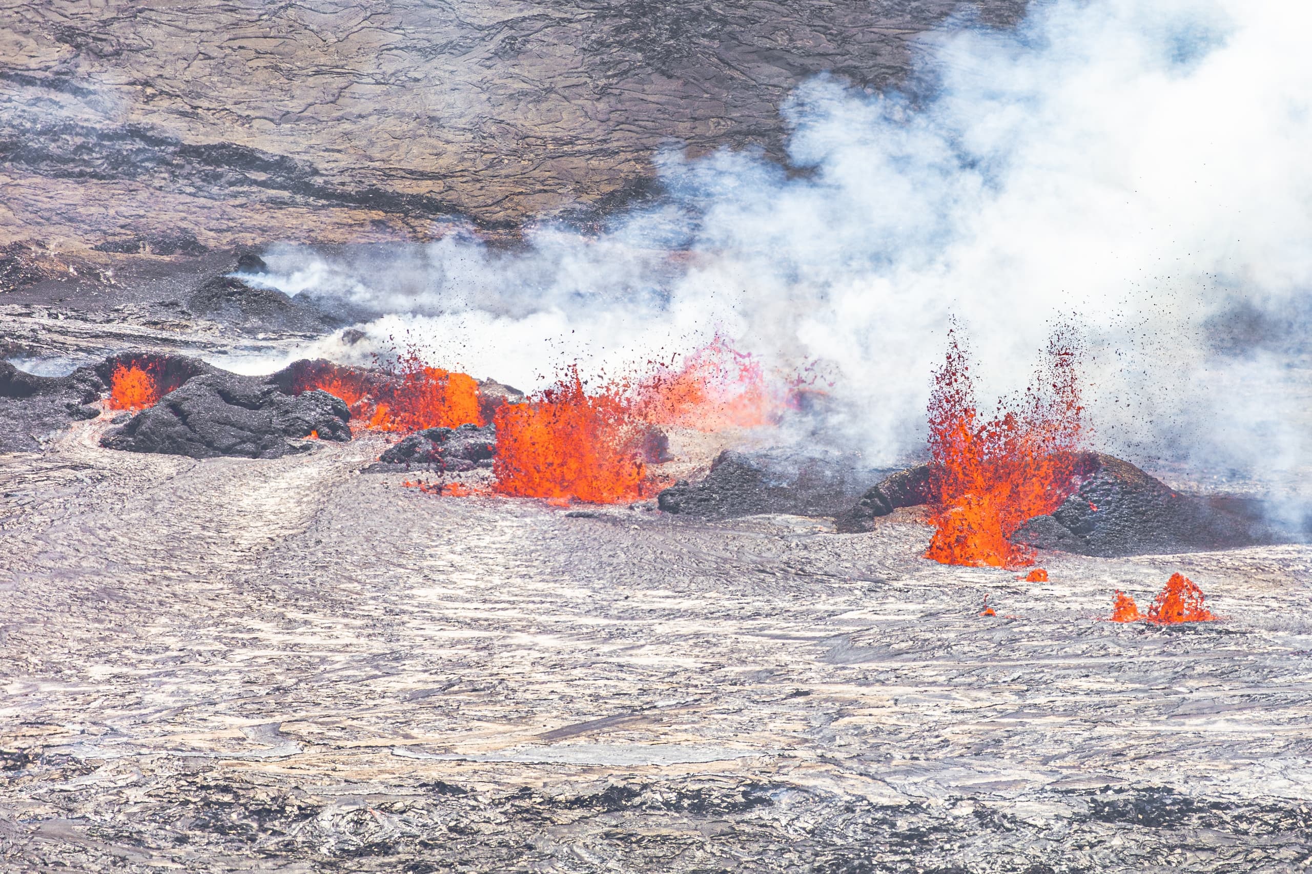 Molten lava flow with steam venting across rocky coastal lava field